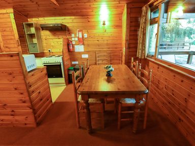 A dining area with a wooden table and six chairs next to a kitchen in a wooden cabin at Partridge Withern near Alford