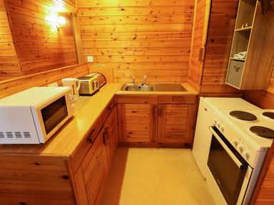 A small kitchen with wooden cabinets microwave kettle toaster sink and electric stove at Partridge in Withern near Alford