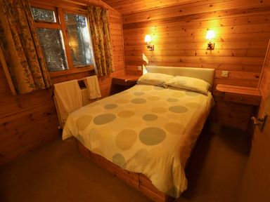 A bedroom with a double bed and wooden walls with bedside shelves and wall lamps at Partridge in Withern near Alford