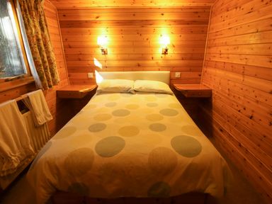 A bedroom with a bed and side tables with lamps on a wooden wall at Partridge in Withern near Alford