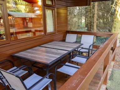 An outdoor wooden deck with a rectangular table and six chairs surrounded by trees at Partridge Withern near Alford
