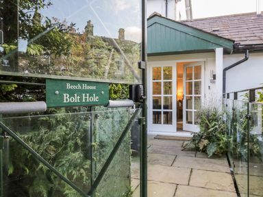 An entrance gate with a green sign reading Beech House Bolt Hole opening to a path leading to a white house with glass doors at The Bolt Hole in Kendal