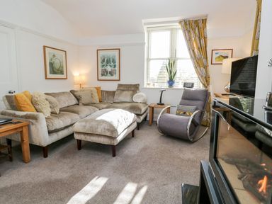 A living room with a beige sofa and a gray armchair near a window with yellow curtains at The Bolt Hole in Kendal