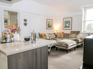 A living room with a sectional sofa a coffee pot a kettle on a countertop and framed pictures on the wall at The Bolt Hole in Kendal
