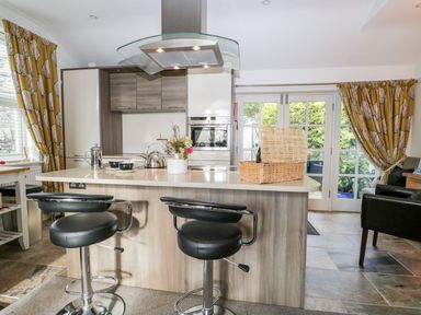 A kitchen with an island featuring two black bar stools and a wicker basket at The Bolt Hole in Kendal