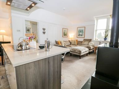 A kitchen island with kettle and coffee press next to a living room with a sectional sofa and framed pictures at The Bolt Hole in Kendal