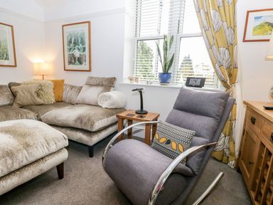 A living room with a gray armchair a beige sofa a wooden side table and a window with yellow curtains at The Bolt Hole in Kendal