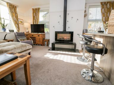 A living room with a fireplace a television armchair and bar stools at The Bolt Hole in Kendal