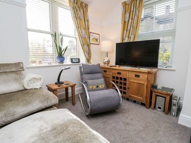 A living room with a gray chair a beige couch wooden side tables a wooden TV cabinet and a television at The Bolt Hole in Kendal