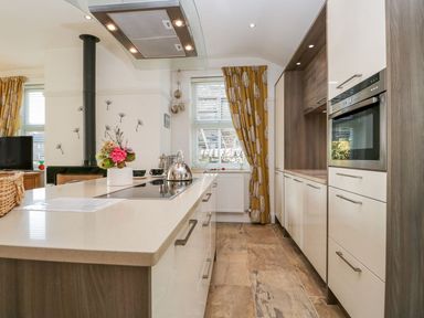 A kitchen with a countertop island a stove kettle and oven with yellow curtains at The Bolt Hole in Kendal
