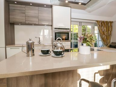 A kitchen with a countertop holding a coffee pot two cups a kettle and a vase with flowers at The Bolt Hole in Kendal