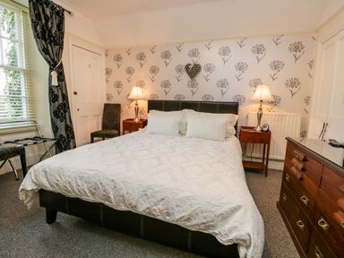 A bedroom with a bed two bedside tables with lamps a chair a window with curtains and a chest of drawers at The Bolt Hole in Kendal