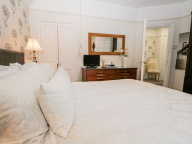 A bedroom with a bed pillows and lamp a wooden dresser with a mirror and a TV a chair in an adjacent room at The Bolt Hole in Kendal
