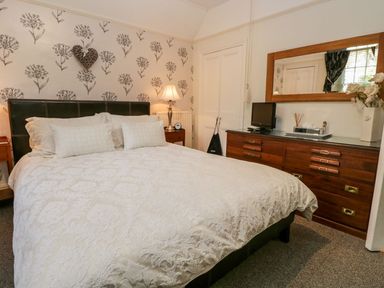 A bedroom with a large bed a wooden dresser with a mirror and a small television at The Bolt Hole in Kendal