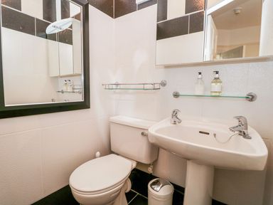 A bathroom with a toilet sink two mirrors soap dispensers and a trash bin at The Bolt Hole in Kendal