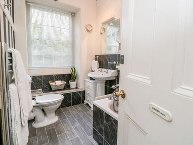 A bathroom with a toilet, sink, bathtub, window with blinds, towel rack, and a plant at The Bolt Hole in Kendal