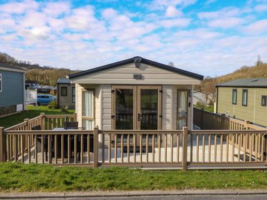 A beige mobile home with a wooden deck and outdoor furniture surrounded by a fence at 98 The Heron in New Quay
