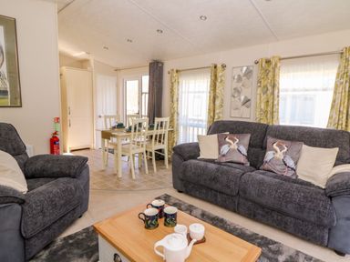 A living room with gray sofas and bird cushions with a wooden coffee table and dining table with chairs at 98 The Heron in New Quay