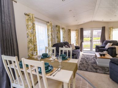 A dining table set with dishes and glassware next to a living room with sofas and coffee table at 98 The Heron in New Quay