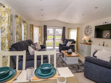 A living room with grey sofas a coffee table and dining table with blue plates at 98 The Heron in New Quay