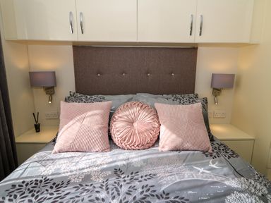 A bed with pink and gray pillows and a floral patterned duvet in a bedroom at 98 The Heron in New Quay