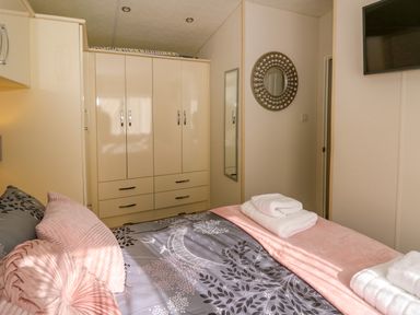 A bedroom with a bed with folded towels and cushions and a wardrobe at 98 The Heron in New Quay