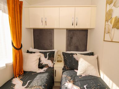 A bedroom with two single beds with patterned bedding and orange curtains at 98 The Heron in New Quay