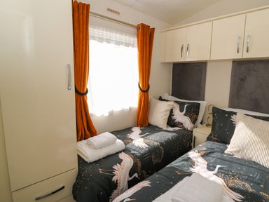 A bedroom with two single beds with bird-patterned bedding and orange curtains at 98 The Heron in New Quay