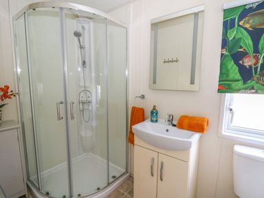 A bathroom with a corner shower enclosure a sink with orange towels and a mirror at 98 The Heron in New Quay