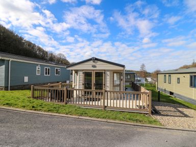 A mobile home with a fenced porch and outdoor furniture on a grassy plot at 98 The Heron in New Quay