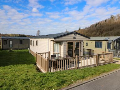 A beige mobile home with a fenced patio and outdoor furniture on grass at 98 The Heron in New Quay