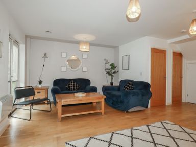 A living room with two blue sofas a wooden coffee table a black chair and wooden flooring at Treburgett Porthtowan