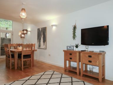 A dining area with wooden table and chairs and a wall-mounted television above two wooden cabinets at Treburgett in Porthtowan