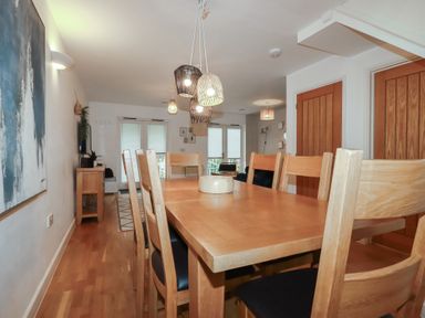 A dining room with a wooden table and chairs with pendant lights above at Treburgett in Porthtowan