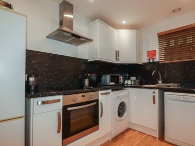 A kitchen with white cabinets a washing machine an oven a microwave and a dishwasher at Treburgett in Porthtowan