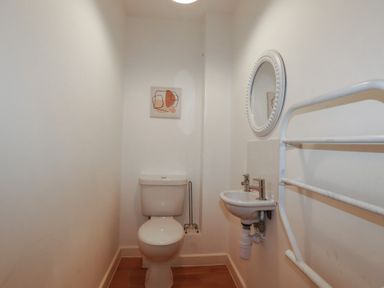 A small bathroom with a toilet a wall-mounted sink a round mirror and a towel rack at Treburgett in Porthtowan