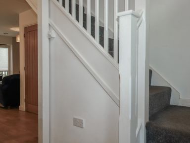 A carpeted staircase with white banisters next to a wooden door and a room with a window at Treburgett in Porthtowan