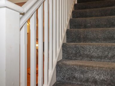 A carpeted staircase with white wooden railing at Treburgett in Porthtowan