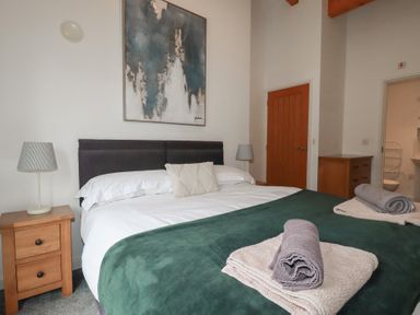 A bedroom with a double bed green blanket bedside tables lamps wooden door and an open bathroom door at Treburgett in Porthtowan