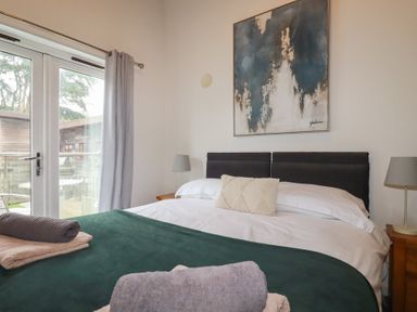 A bedroom with a bed a green blanket and towel stacks next to a window with curtains at Treburgett Porthtowan