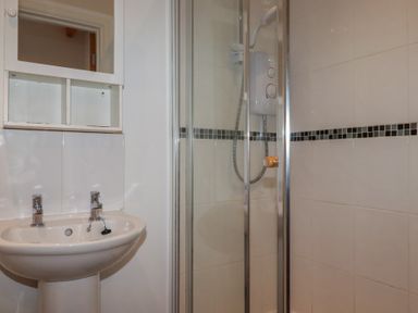 A bathroom with a pedestal sink a wall-mounted cabinet and a glass shower enclosure with an electric shower at Treburgett in Porthtowan