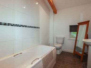 A bathroom with a bathtub, toilet, pedestal sink, standing mirror, and a small window at Treburgett in Porthtowan