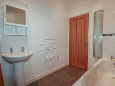 A bathroom with a sink pedestal mirror towel rail wooden door and bathtub at Treburgett Porthtowan