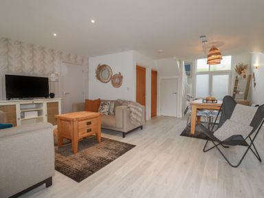 A living room with a television on a cabinet a beige sofa orange cushion and wood table at Trenethick in Porthtowan