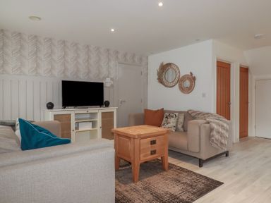 A living room with two sofas a wooden table a television on a cabinet and circular wall mirrors at Trenethick in Porthtowan