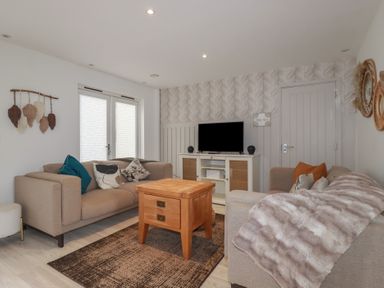 A living room with two beige sofas a wooden coffee table a rug and a television on a cabinet at Trenethick in Porthtowan