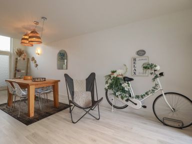 A dining area with wooden table and chairs next to a butterfly chair and a white bicycle adorned with flowers at Trenethick in Porthtowan