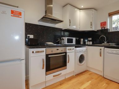A kitchen with white cabinets black countertops and wooden floor at Trenethick in Porthtowan