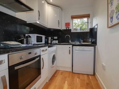 A kitchen with white cabinets black countertops a washing machine oven microwave and dishwasher at Trenethick Porthtowan