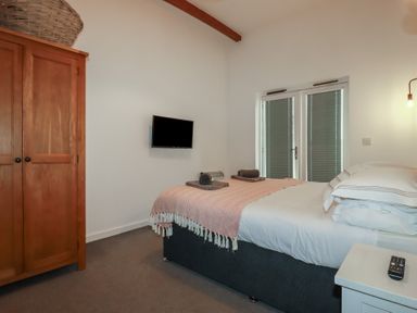 A bedroom with a bed towels on the bed a wooden wardrobe and a wall mounted tv at Trenethick in Porthtowan